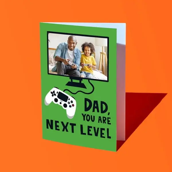 A personalised Fathers Day card with a photo inside a gaming screen design and text reading Dad you are next level, displayed against a bright orange background.